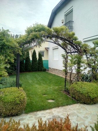 Boltíves pergola, amelyet lilaakác fut be, és amely a kertbe vezet.